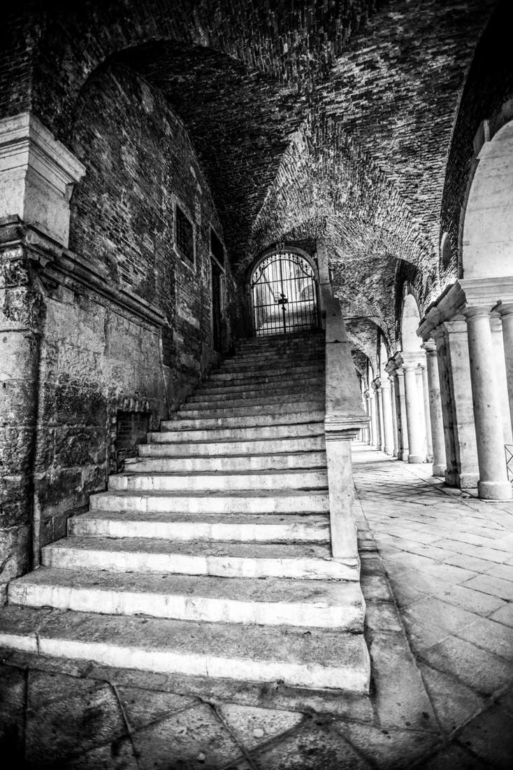 Stone stairs under a brick vault toward an iron gate