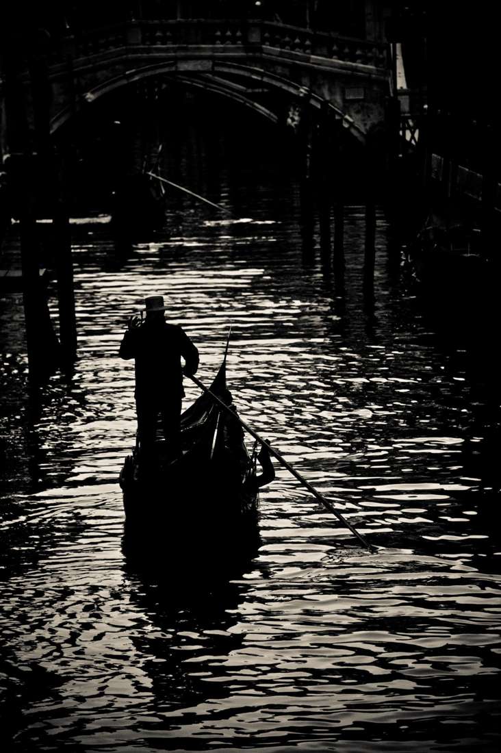 A gondolier in silhouette under a stone bridge