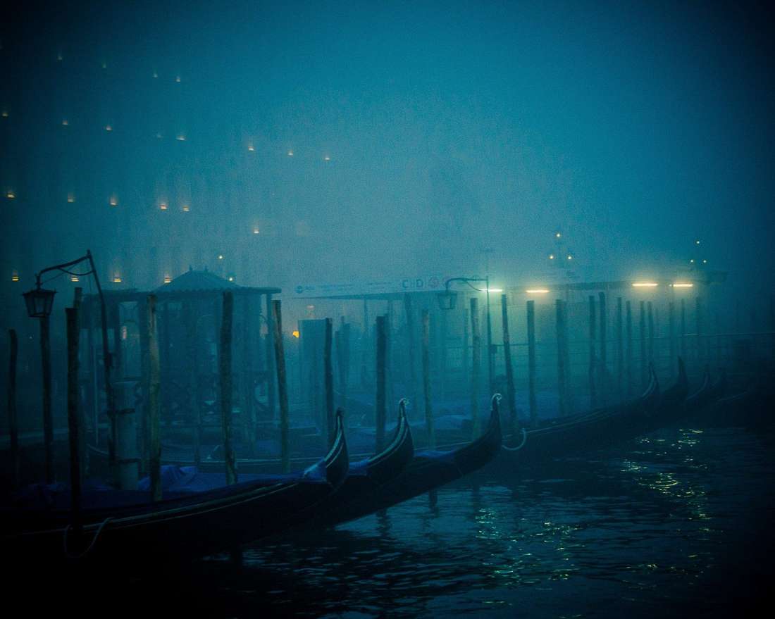 Gondola prows in fog at night, a figure between the boats