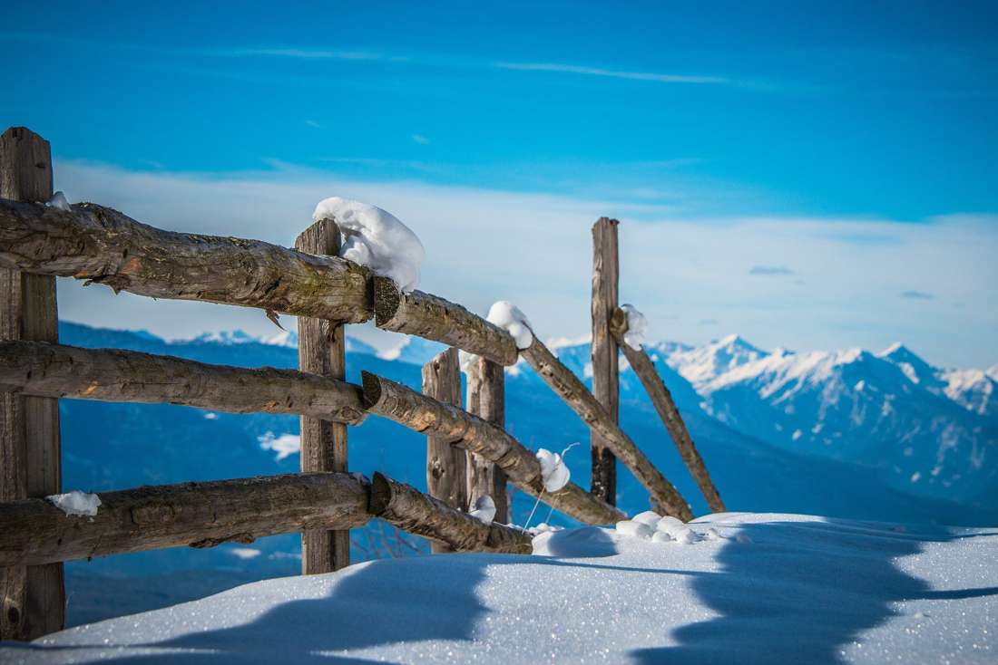 A snow-covered fence with mountains behind