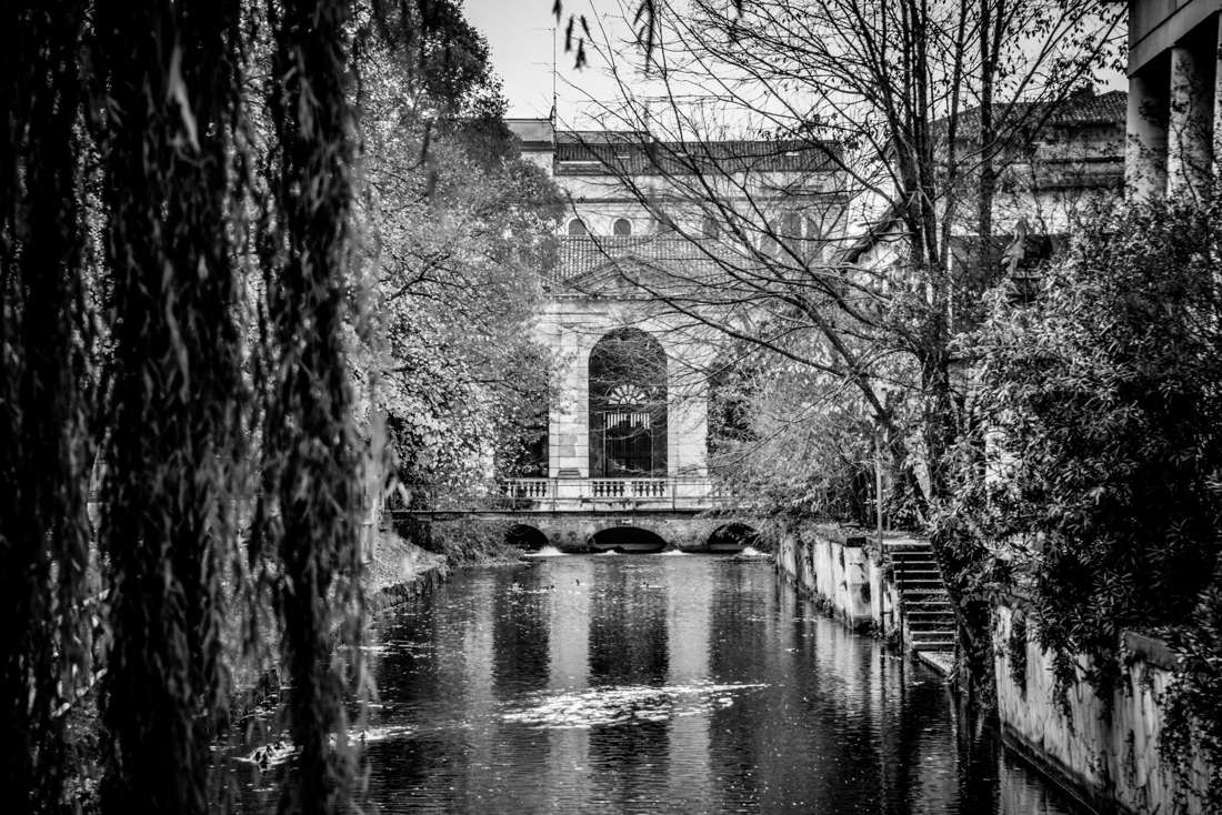 A canal framed by willows and an arched building